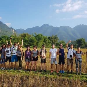 Eine WeRoad Gruppe posiert für ein Foto auf einem goldenen Feld vor grünen Bergen unter blauem Himmel.