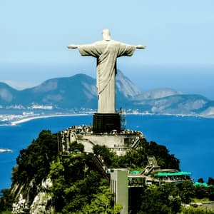 Une grande statue aux bras tendus se dresse sur un sommet de montagne verdoyant, dominant un littoral étendu et une vaste baie bleue.