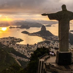 La statue du Christ Rédempteur domine une ville côtière, une baie et des montagnes au coucher du soleil doré.