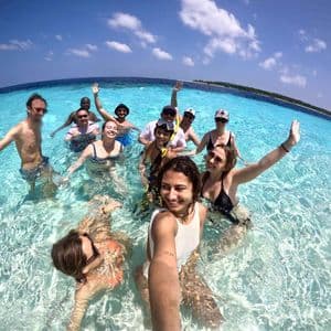 Un groupe WeRoad prend un selfie en nageant ensemble dans une eau océanique claire et turquoise sous un ciel bleu.