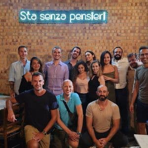 Un viaje en grupo de WeRoad posando para una foto dentro de un restaurante con una pared de ladrillo y un letrero de neón azul de fondo.