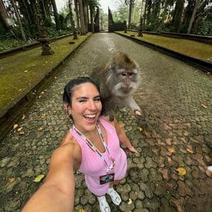 A woman on a WeRoad trip smiles while taking a selfie with a monkey perched on her shoulder on a paved path.