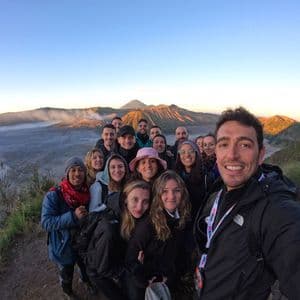A WeRoad group trip takes a selfie on a viewpoint, with a volcanic caldera landscape in the background at sunrise.