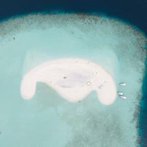 Vue aérienne d'un banc de sable blanc dans des eaux océaniques turquoises, avec des gens se relaxant et des bateaux amarrés à proximité.
