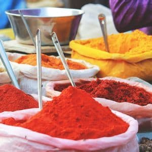 Especias molidas de colores exhibidas en sacos abiertos con cucharones de metal en un mercado.