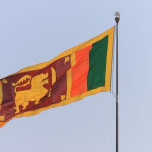 La bandera de Sri Lanka ondeando en un mástil contra un cielo azul claro.
