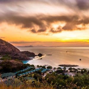 Vue en plongée à longue exposition d'une ville côtière et d'une grande colline près d'une baie au coucher de soleil doré.