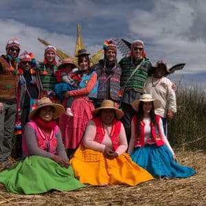 Eine WeRoad Gruppenreise posiert für ein Foto mit Einheimischen in farbenfroher traditioneller Kleidung auf einem Schilfbett.