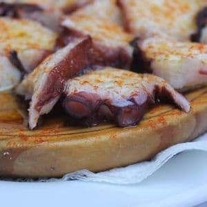 Primer plano de pulpo en rodajas sazonado con pimentón y aceite de oliva, servido en un plato redondo de madera tradicional.