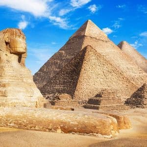 Le Grand Sphinx trône dans le désert avec les Pyramides de Gizeh en arrière-plan sous un ciel bleu.