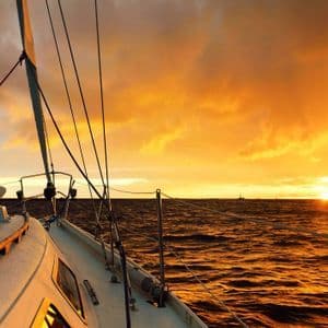 Vista dal ponte di una barca a vela sull'oceano aperto durante un tramonto vibrante e nuvoloso.