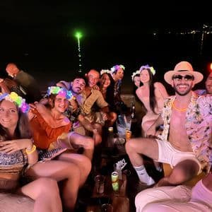 Un grupo de WeRoad posa para una foto durante una fiesta nocturna en la playa, luciendo festivas coronas de flores luminosas.