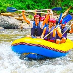 Un groupe WeRoad sourit et lève ses pagaies en faisant du rafting en eaux vives sur une rivière.