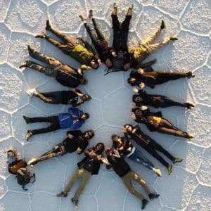 Luftaufnahme einer WeRoad-Gruppe, die im Kreis auf einer riesigen Salzwüste mit polygonalen Rissen liegt.
