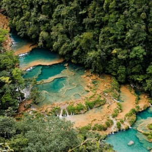 Eine Luftaufnahme von türkisfarbenem Flusswasser, das über terrassierte Becken und Wasserfälle fließt, umgeben von dichtem grünen Dschungel.