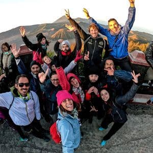 Un grupo de WeRoad posando para una selfie en un mirador, con un gran volcán visible de fondo al amanecer.