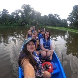 Un gruppo WeRoad in viaggio, con giubbotti di salvataggio, si scatta un selfie su una barca blu mentre naviga lungo un fiume circondato da una fitta giungla.
