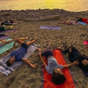 Un viaggio di gruppo WeRoad sdraiati sugli asciugamani su una spiaggia di sabbia, facendo esercizi di stretching al tramonto.
