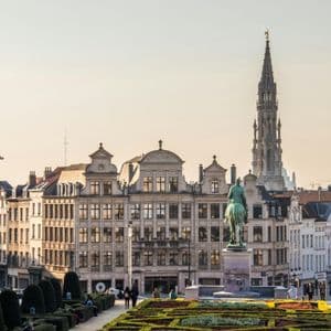 Una plaza de la ciudad con jardines formales, una estatua ecuestre y edificios históricos con una alta aguja gótica al fondo.