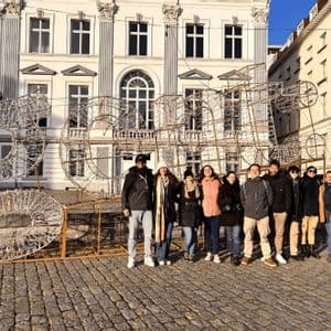 Un grupo de WeRoad posa en una calle empedrada frente a una gran instalación de luces y un edificio clásico.