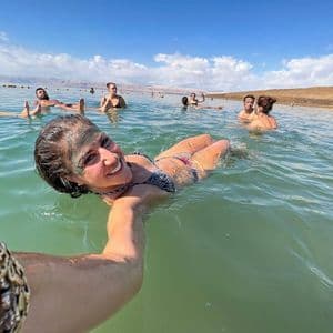 Une femme souriante, le visage couvert de boue, prend un selfie tout en flottant dans l'eau lors d'un voyage de groupe WeRoad.