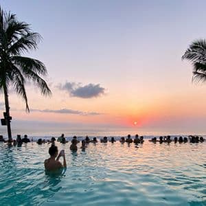 Un viaggio di gruppo WeRoad osserva il tramonto da una piscina a sfioro con vista sull'oceano, incorniciata da palme.