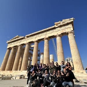 Un viaggio di gruppo WeRoad in posa per una foto davanti a un antico tempio con grandi colonne sotto un cielo azzurro chiaro.