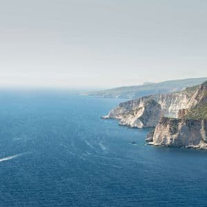 Ein Schnellboot erzeugt eine weiße Bugwelle auf dem tiefblauen Meer, während es eine dramatische Küstenlinie mit weißen Klippen passiert.