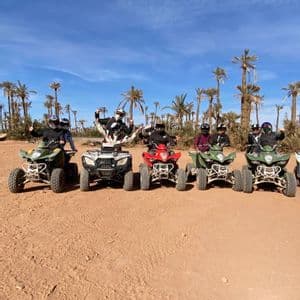 Un viaje en grupo de WeRoad posando en sus quads en un paisaje desértico con un palmeral de fondo.