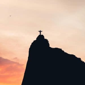 La estatua del Cristo Redentor recortada en una cima montañosa contra un atardecer de colores vivos.