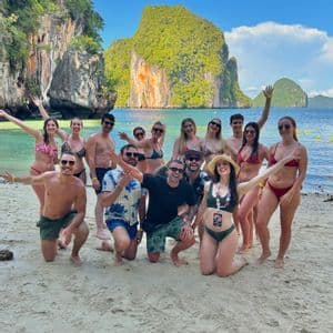 A WeRoad group trip in swimwear posing for a photo on a sandy beach with green rocky islands in the background.