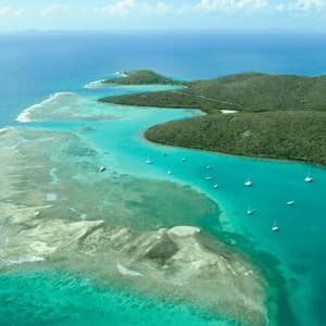 Una vista aerea di una penisola insulare verde e tropicale con barche a vela ancorate nelle calme acque turchesi di una baia.