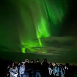 Un groupe WeRoad en voyage, posant la nuit dans un paysage enneigé sous les aurores boréales vertes.