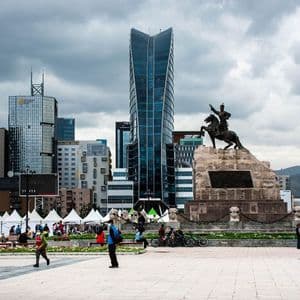 Eine Reiterstatue auf einem großen Steinsockel auf einem Stadtplatz, mit modernen Wolkenkratzern im Hintergrund unter einem bewölkten Himmel.