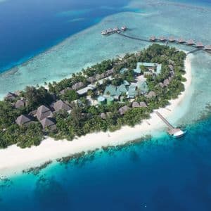 An aerial view of a tropical island resort with white sand beaches, lush palm trees, and overwater villas on turquoise water.