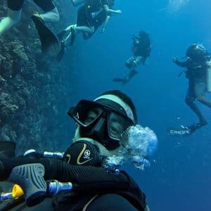 Un hombre se toma una selfie bajo el agua mientras bucea con un viaje en grupo de WeRoad junto a una pared de coral.