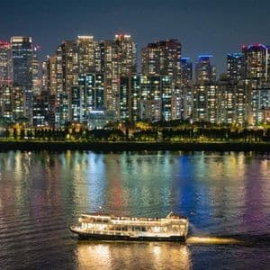 Una barca illuminata naviga di notte su un fiume, di fronte a uno skyline cittadino illuminato.