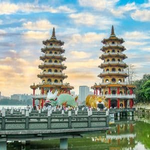 Due pagode ornate con ingressi di drago e tigre si ergono su un lago, con uno skyline cittadino e un cielo nuvoloso sullo sfondo.