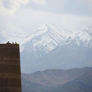 A WeRoad group trip sits on top of a historic brick tower, with a vast, snow-capped mountain range in the background.