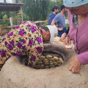 Un uomo si sporge in un grande forno tandoor in argilla per adagiare l'impasto del pane sulle sue pareti, osservato da una donna e da un gruppo WeRoad in viaggio.