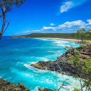Veduta panoramica di costa tropicale con acqua turchese, spiaggia di sabbia e colline verdi.