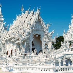 An ornate, all-white temple complex with intricate carvings and spires stands against a clear, deep blue sky.