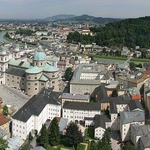 Una vista panoramica dall'alto di una storica città europea con una grande cattedrale, un fiume e una collina boscosa sullo sfondo.