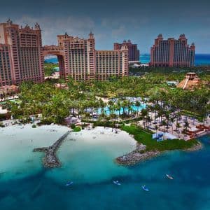Veduta aerea di un grande resort tropicale con hotel rosa, una spiaggia di sabbia bianca, una laguna turchese e numerose palme.