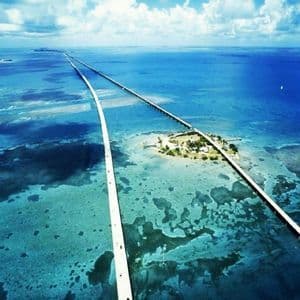 Una vista aerea di due lunghi ponti che si estendono su acque oceaniche turchesi, collegandosi a una piccola isola verde.