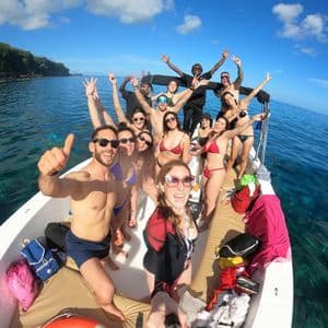 Un gruppo WeRoad sorride e posa per un selfie grandangolare su una barca in acqua limpida e turchese.