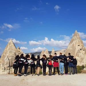 Rear view of a WeRoad group trip with arms around each other, admiring conical rock formations under a blue sky.
