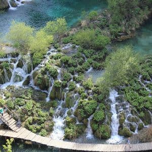 Eine Luftaufnahme von Menschen, die auf einem Holzsteg gehen, der sich durch terrassierte Wasserfälle und türkisfarbene Becken schlängelt.