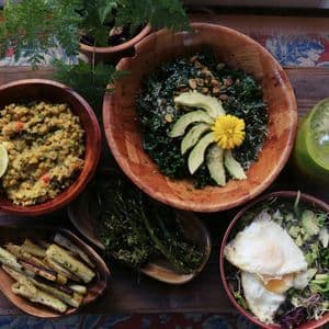 Una veduta dall'alto di un pasto sano e vario, servito in ciotole di legno, che include insalate, verdure arrostite, lenticchie e un frullato verde.