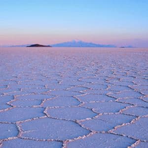Una vasta distesa salina con motivi esagonali si estende verso montagne lontane sotto un cielo colorato all'alba.